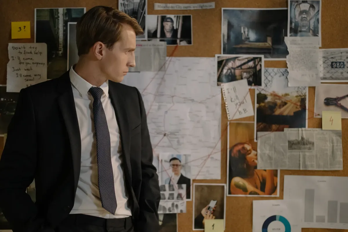 Detective in suit examining evidence on cork board during investigation process.