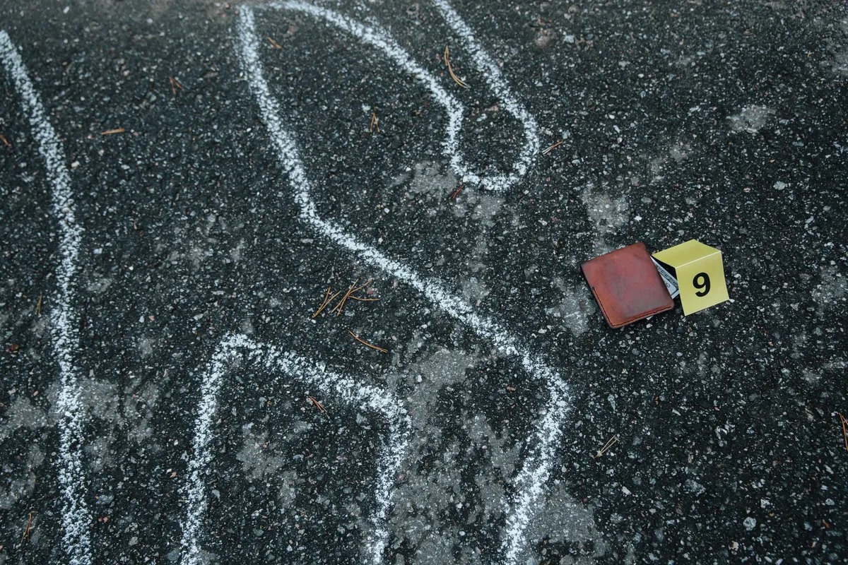 Crime scene with a chalk outline and evidence marker on asphalt.